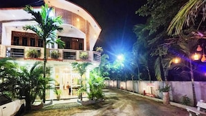 A multi-story building with a curved facade, outdoor seating area, and a car parked in front. - Green star villa (Jaffna)