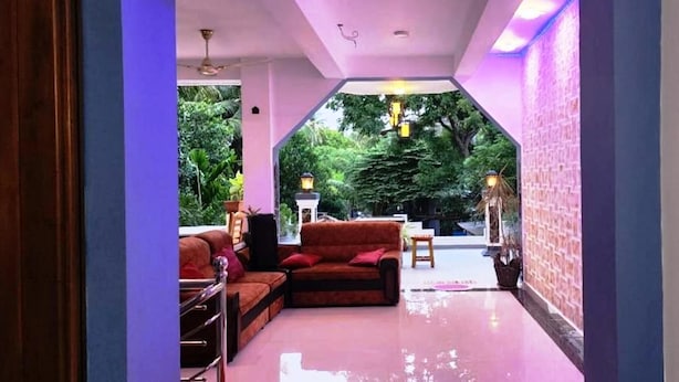 A hallway with a sofa, a small table, and a chair. There are plants and a lamp in the background. - Green star villa (Jaffna)