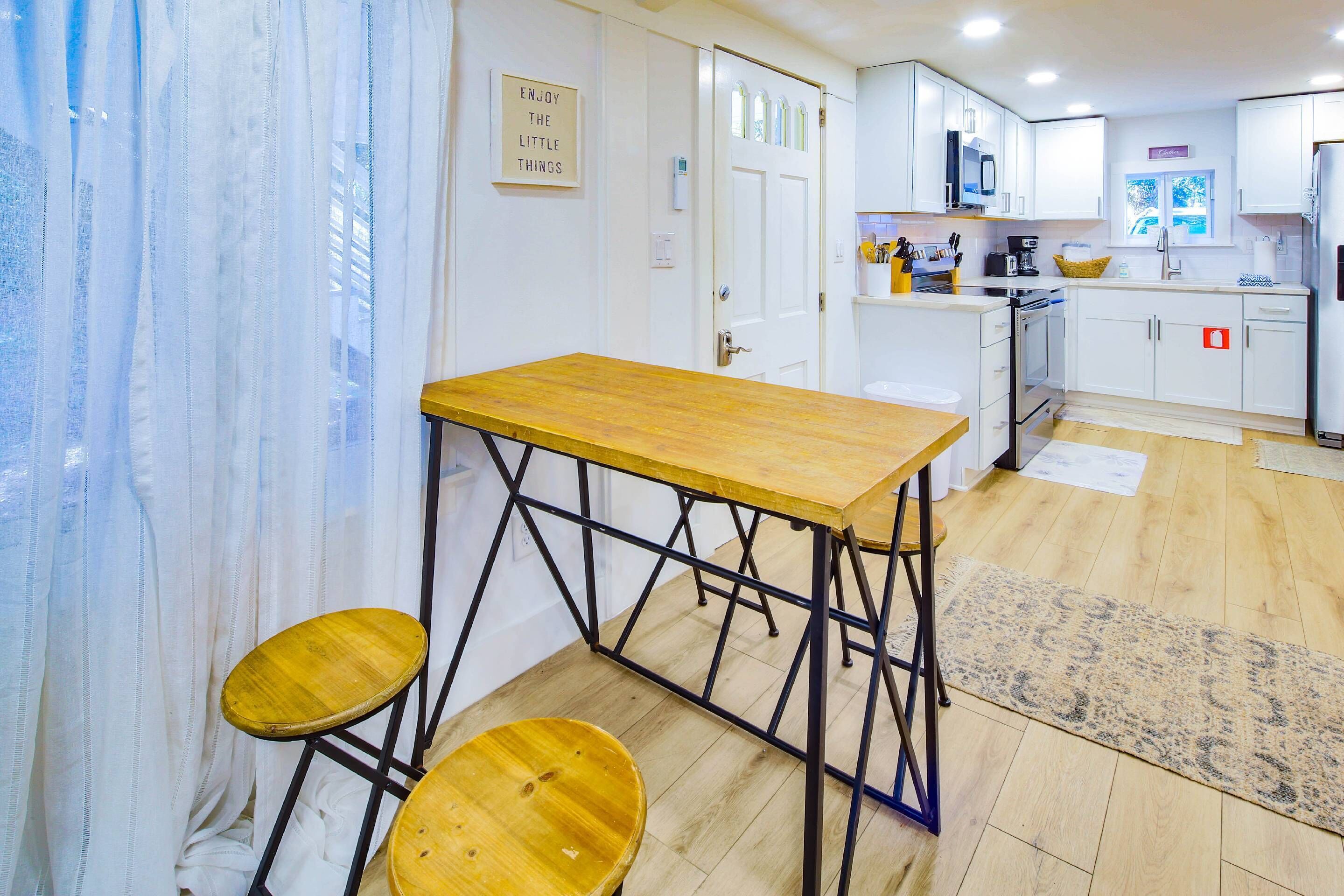 Une cuisine de taille réduite avec des meubles blancs, une table en bois et deux tabourets.