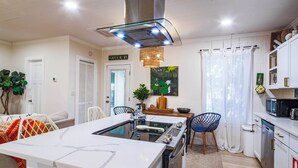 Una cocina moderna con una isla central, armarios blancos, una campana extractora de acero inoxidable y un comedor con mesa y sillas.