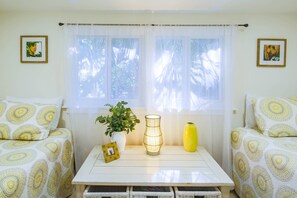 A room with two beds, a table with a vase, a plant, and framed pictures on the walls. - Two Master Suites, Covered Deck & One Block Walk to Beach - Get Your Toes in the Sand in Minutes! (Folly Beach)
