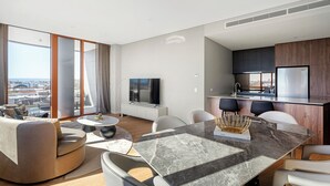 Ein modernes Wohnzimmer mit einem großen Fenster, einem Essbereich mit einem Marmortisch und einer Küche mit dunklen Schränken.