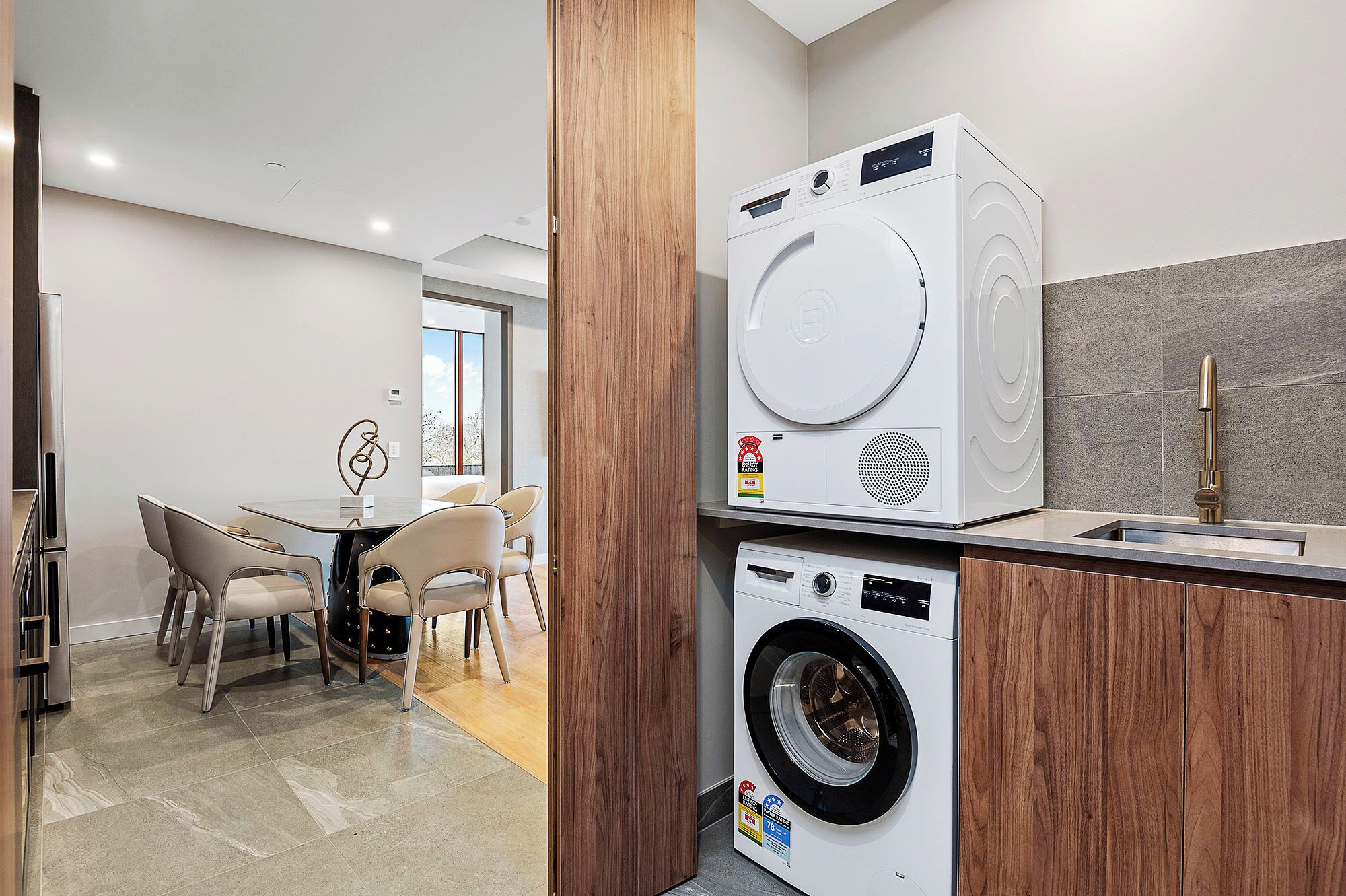 A modern kitchen with a built-in washer and dryer, a dining area with a table and chairs, and a view of the outdoors.