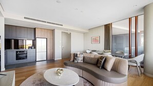 Ein modernes Wohnzimmer mit einer Couch, einem Couchtisch und einer Küchenzeile inklusive Kühlschrank und Backofen.