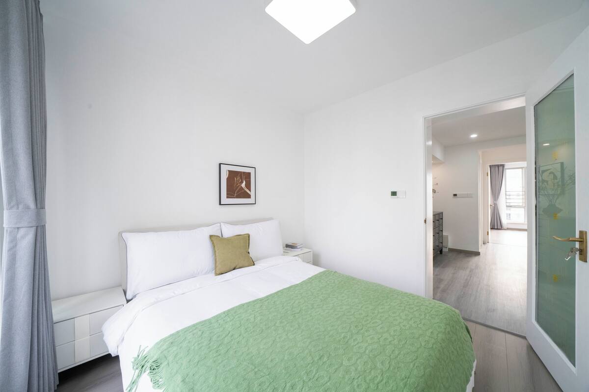 Ein Schlafzimmer mit einem Bett, einem Nachttisch, einem gerahmten Bild an der Wand und einer Tür zu einem anderen Raum.
