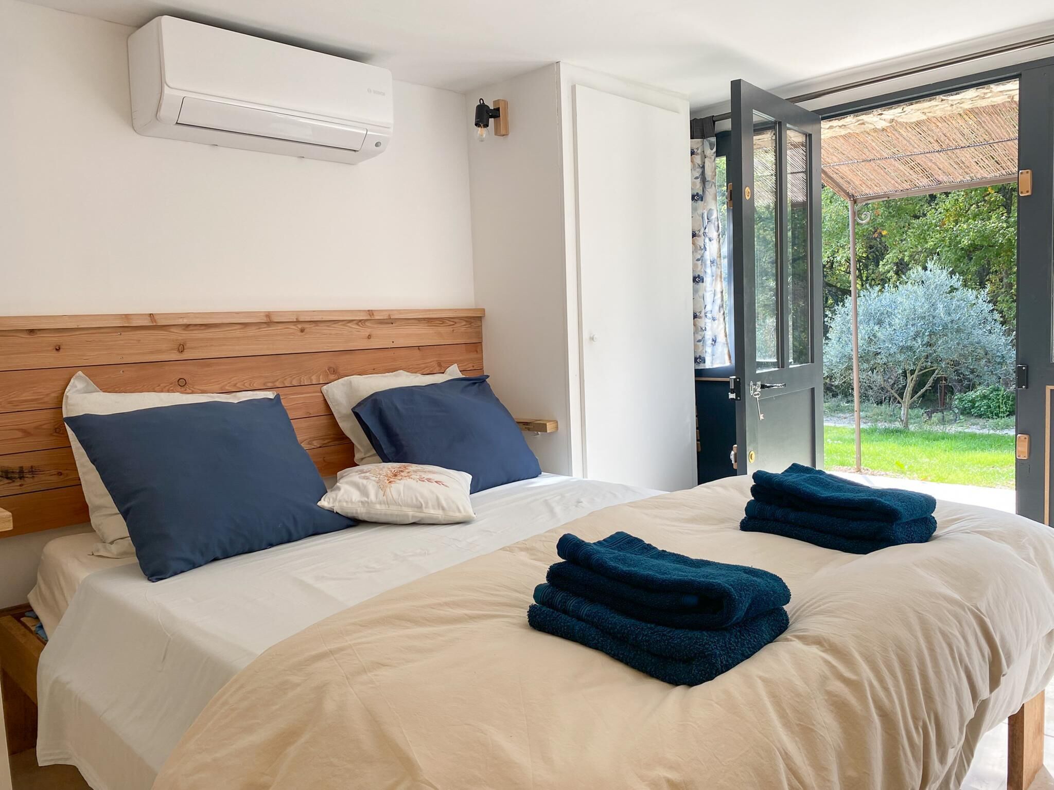 Ein Schlafzimmer mit einem hölzernen Kopfende, einer weißen Klimaanlage und Blick auf einen Garten durch eine offene Tür.