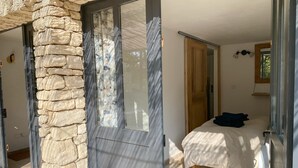 Een slaapkamer met een stenen muur, een bed met een blauw kussen en een raam met gordijnen.