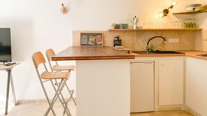 Een kleine keuken met een houten aanrecht, een spoelbak en een eethoekje met een stoel.