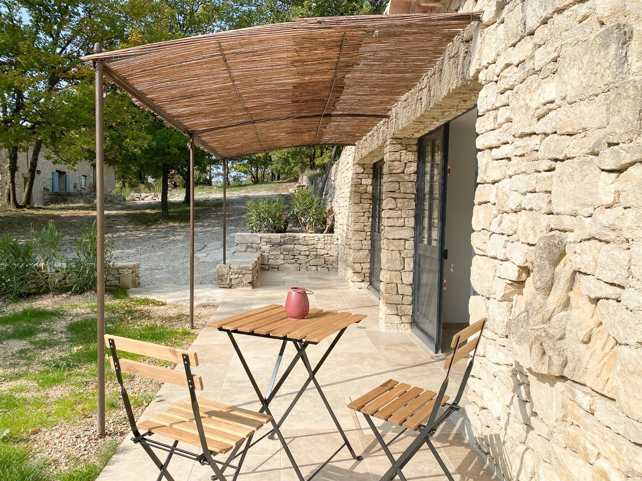 A stone building with a wooden table and chairs under a woven shade.