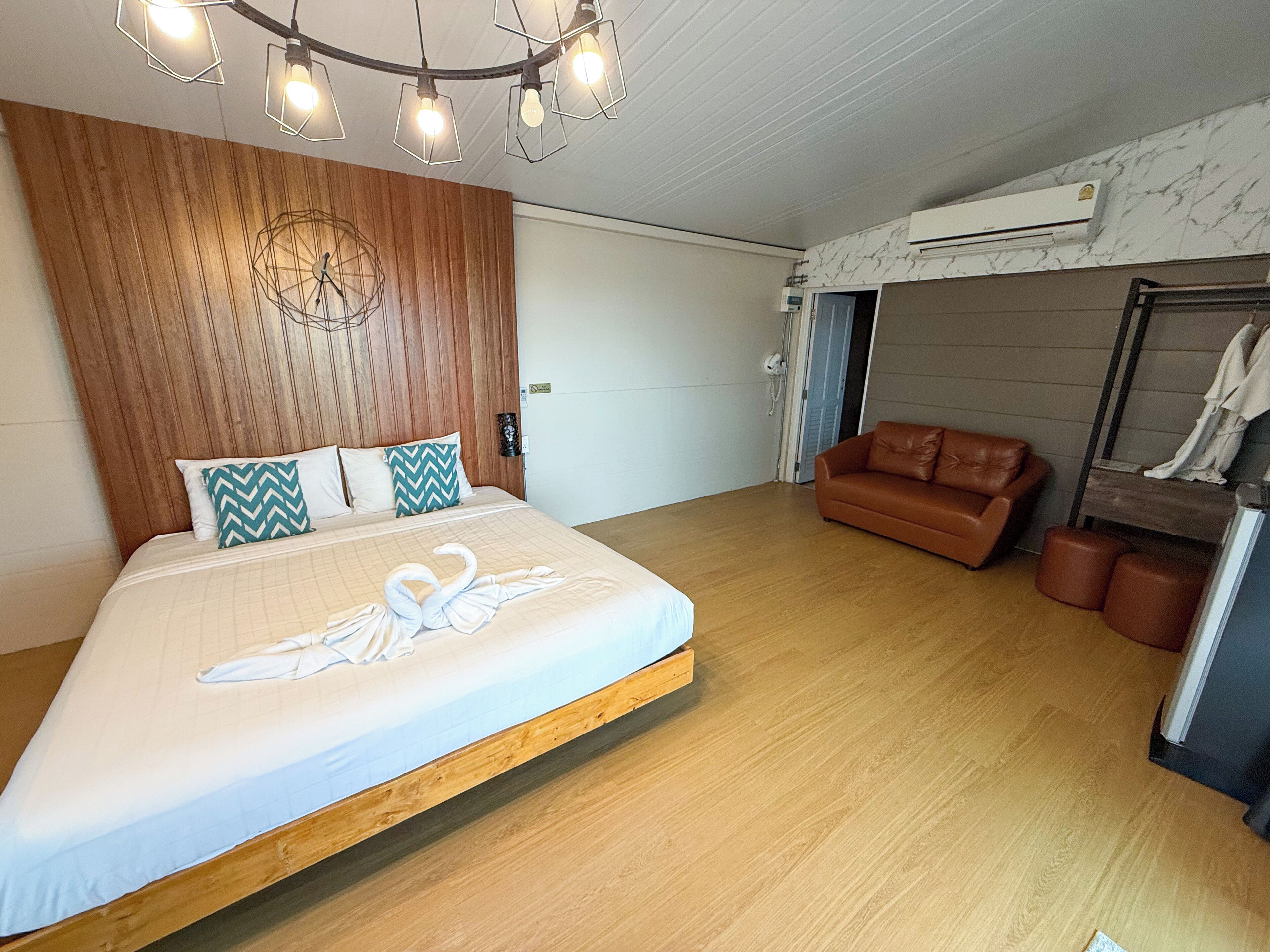 Ein Schlafzimmer mit Bett, Holz-Kopfteil, braunem Ledersofa und Kleiderständer.