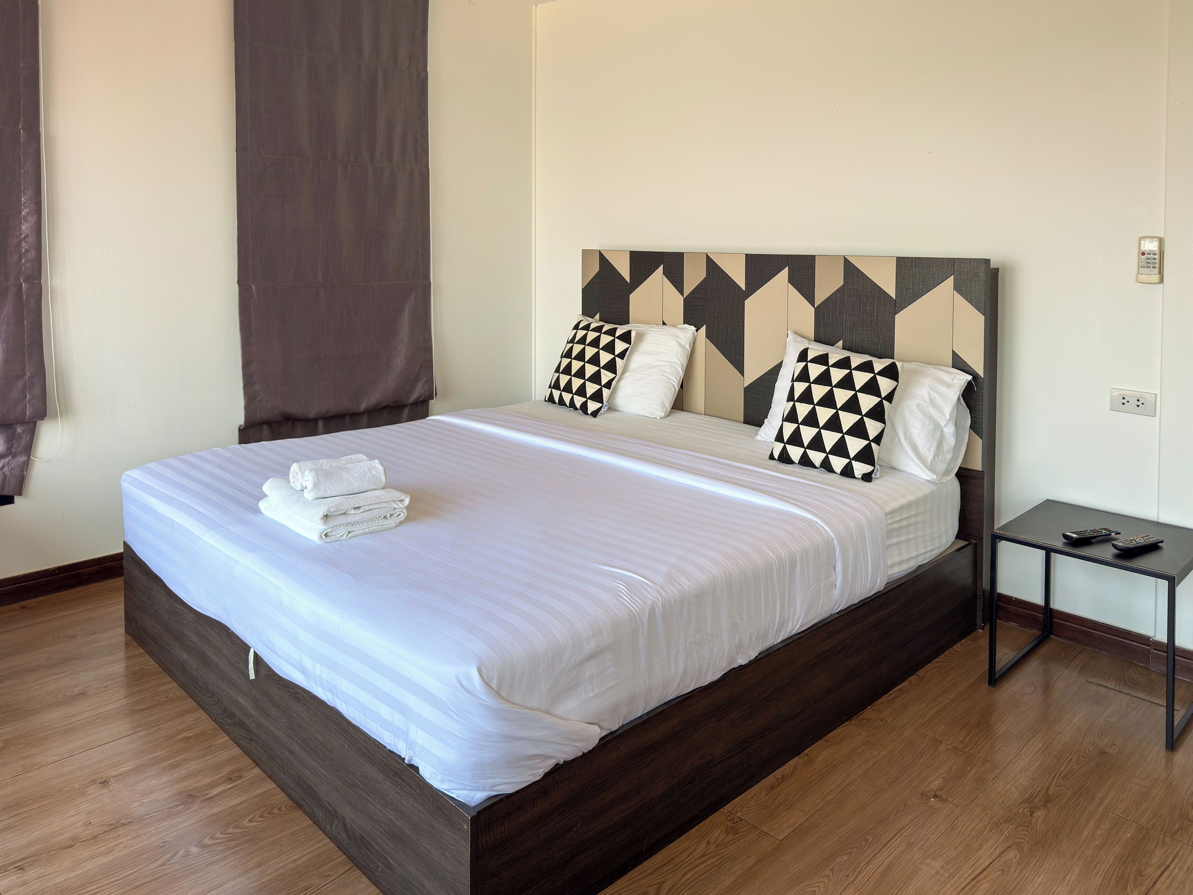 Una cama bien tendida con sábanas blancas y un cabecero con diseño geométrico.