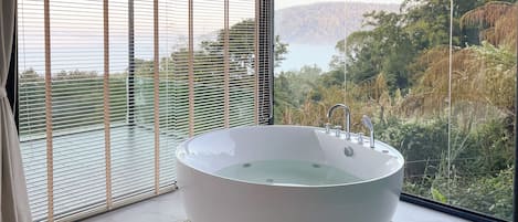 A modern bathroom with a freestanding bathtub, large windows, and a view of a natural landscape.