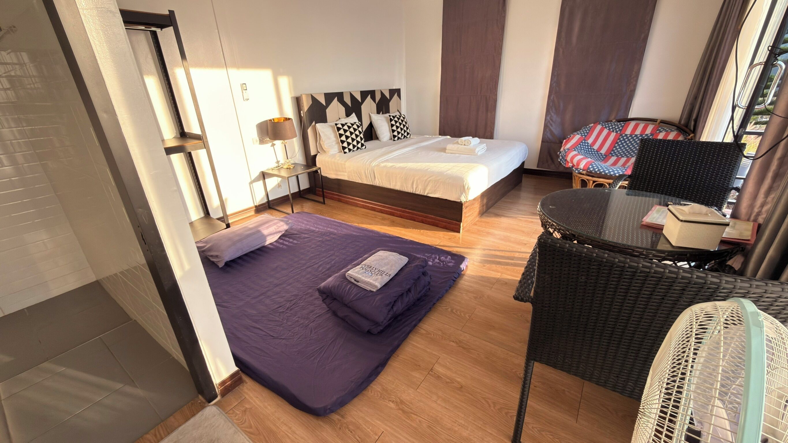 A hotel room with a bed, a small table, a chair, and a window with curtains.