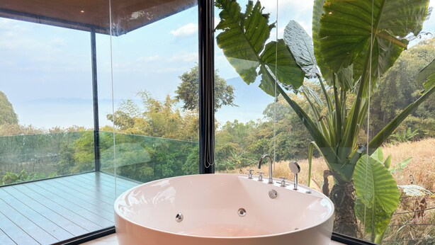 Una tina grande y redonda en un baño moderno con vistas a un jardín exuberante y montañas distantes.