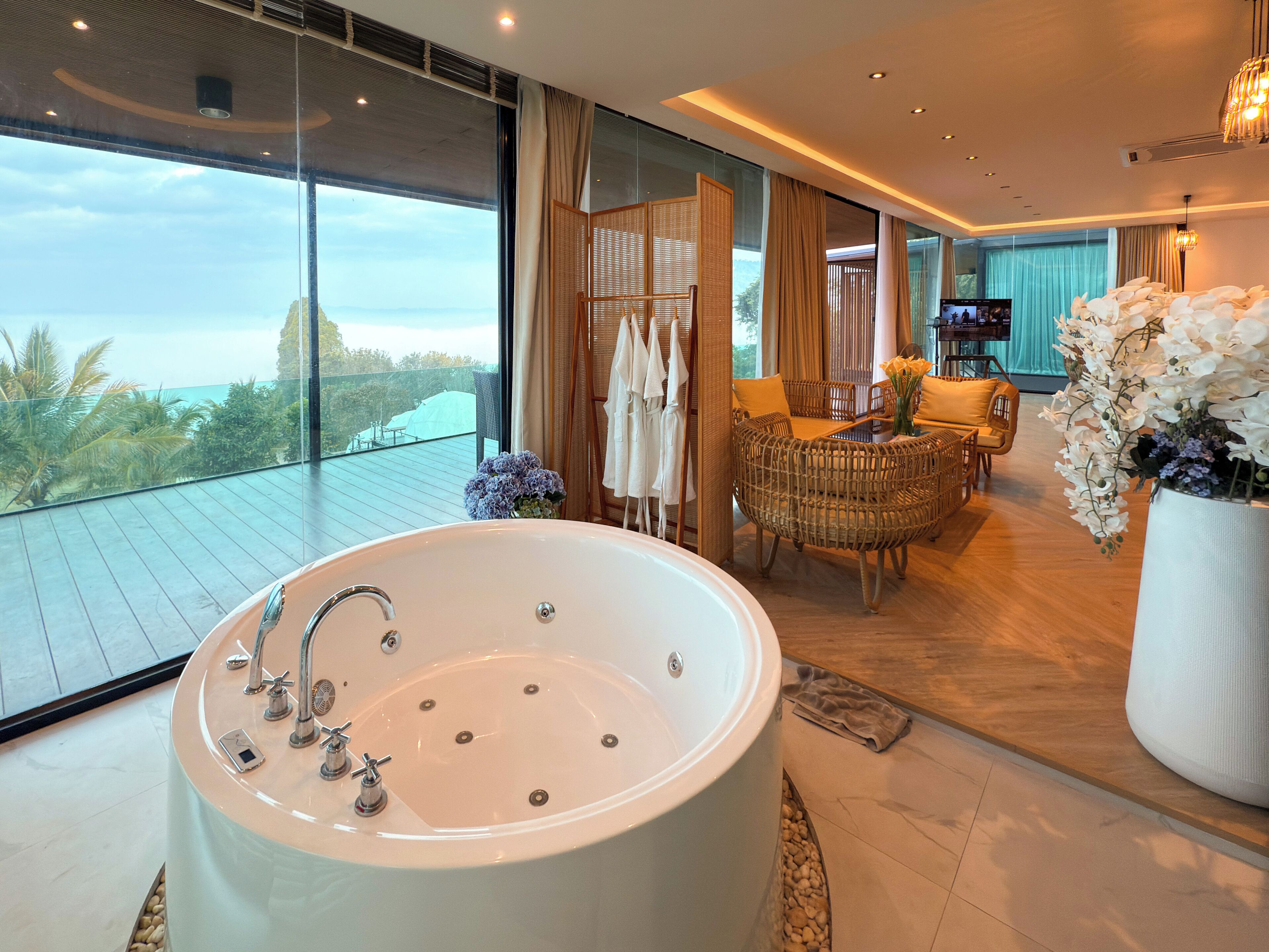 A modern bathroom with a large bathtub, wicker furniture, and a view of the ocean.