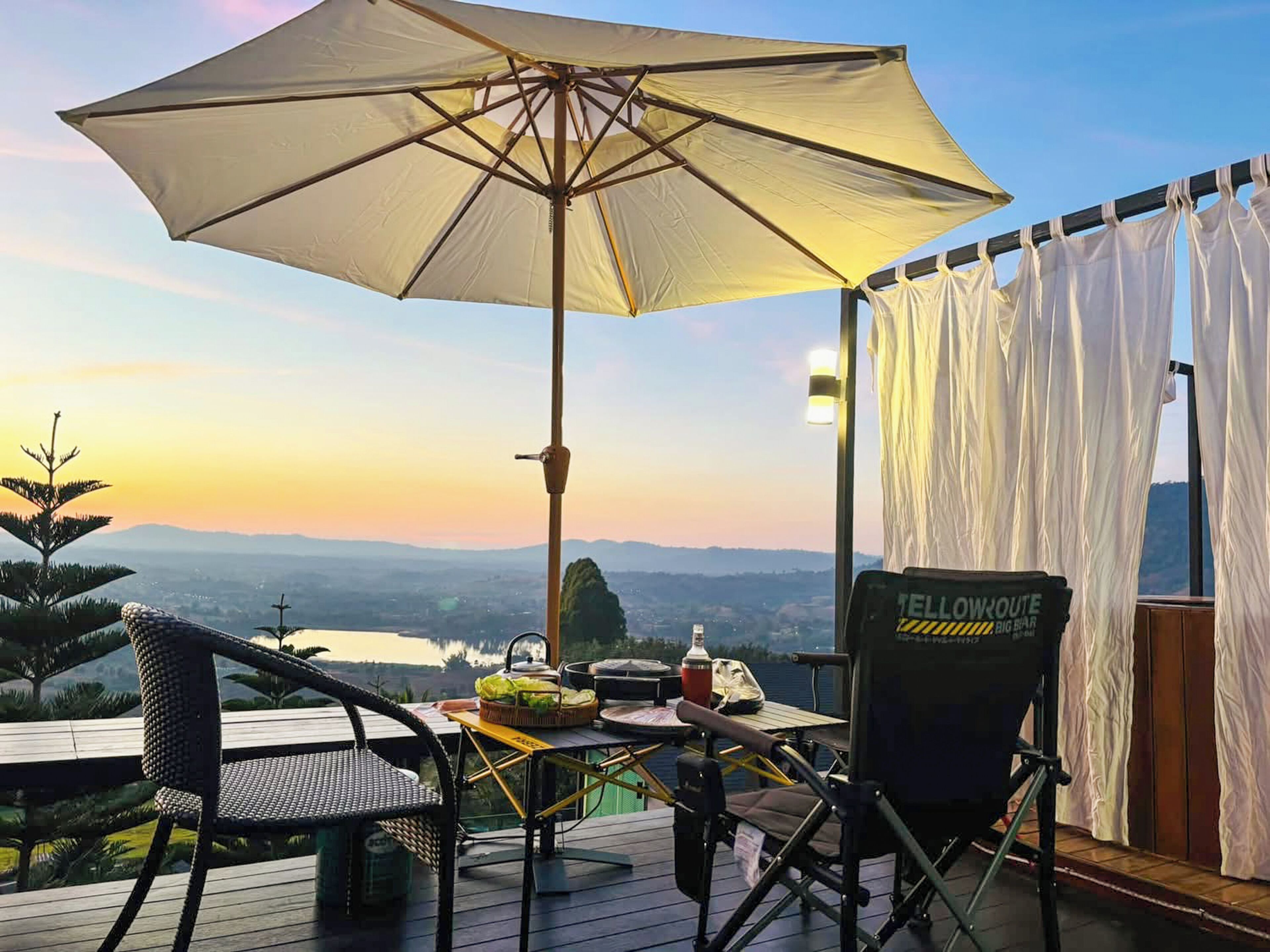 Une terrasse avec une table, des chaises, un parasol et une vue sur un lac et des montagnes.