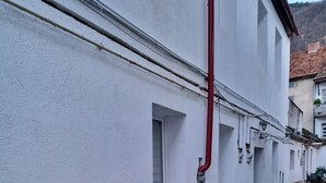 Eine enge Straße mit einem weißen Gebäude, einer roten Rohrleitung und einem kleinen Tisch mit einem Stuhl.