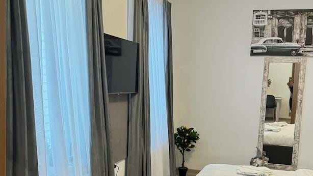 Ein Schlafzimmer mit Bett, Fernseher, Spiegel und einem Fenster mit Vorhängen.