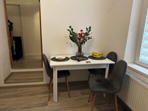 A dining area with a white table, black chairs, a vase with flowers, a bowl of cereal, a plate of bananas, and a cup. - Cosy apartment in a city centre Brasov (Brașov)