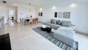 A modern living room with a grey sofa, a dining table with chairs, and a kitchen area in the background. - Tyms Changning 2BR near Zhongshan  Metro (Shanghai)