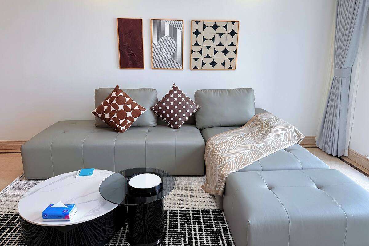 A modern living room with a grey sectional sofa, two patterned throw pillows, a coffee table with a white top and black base, and a black and white patterned rug.