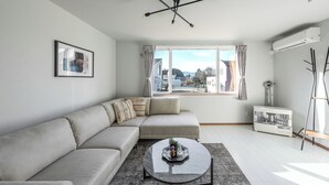 A modern living room with a sectional sofa, a round coffee table, and a large window with curtains. - HILLS NISEKO C (Niseko)