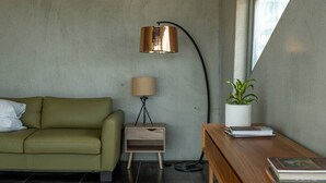 A modern living room with a green sofa, a wooden side table with a lamp, and a potted plant. - Mabels Lookout - Sauna| Bath| Sunsets| Views| Fire (North Bruny)