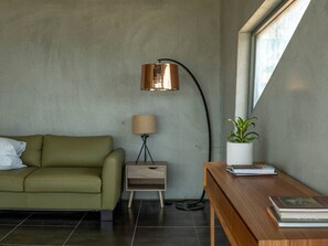Una sala moderna con un sofá verde, una mesita de madera con una lámpara y una planta en maceta.