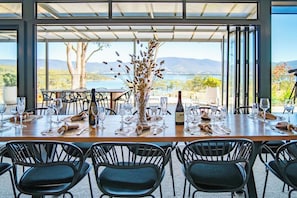 A dining table set for six with chairs, a bottle of wine, and a decorative vase. - Mabels Lookout - Sauna| Bath| Sunsets| Views| Fire (North Bruny)