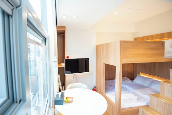 A modern hotel room with a bunk bed, a flat-screen TV, a small round table, and a window with blinds. - AKA STAY Myeongdong (Seoul)