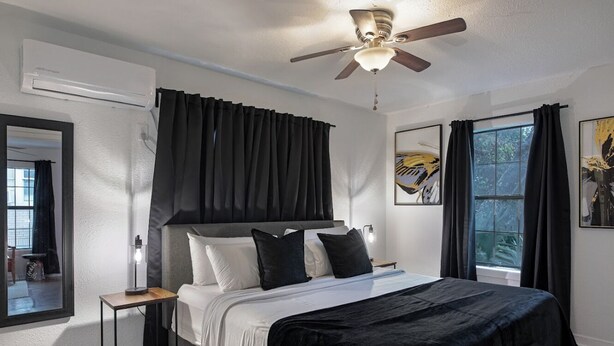 Een moderne slaapkamer met een bed, een plafondventilator, een raam met gordijnen en een wandairconditioner.