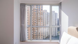 Un dormitorio con un ventanal grande, una cama y vistas de edificios altos.