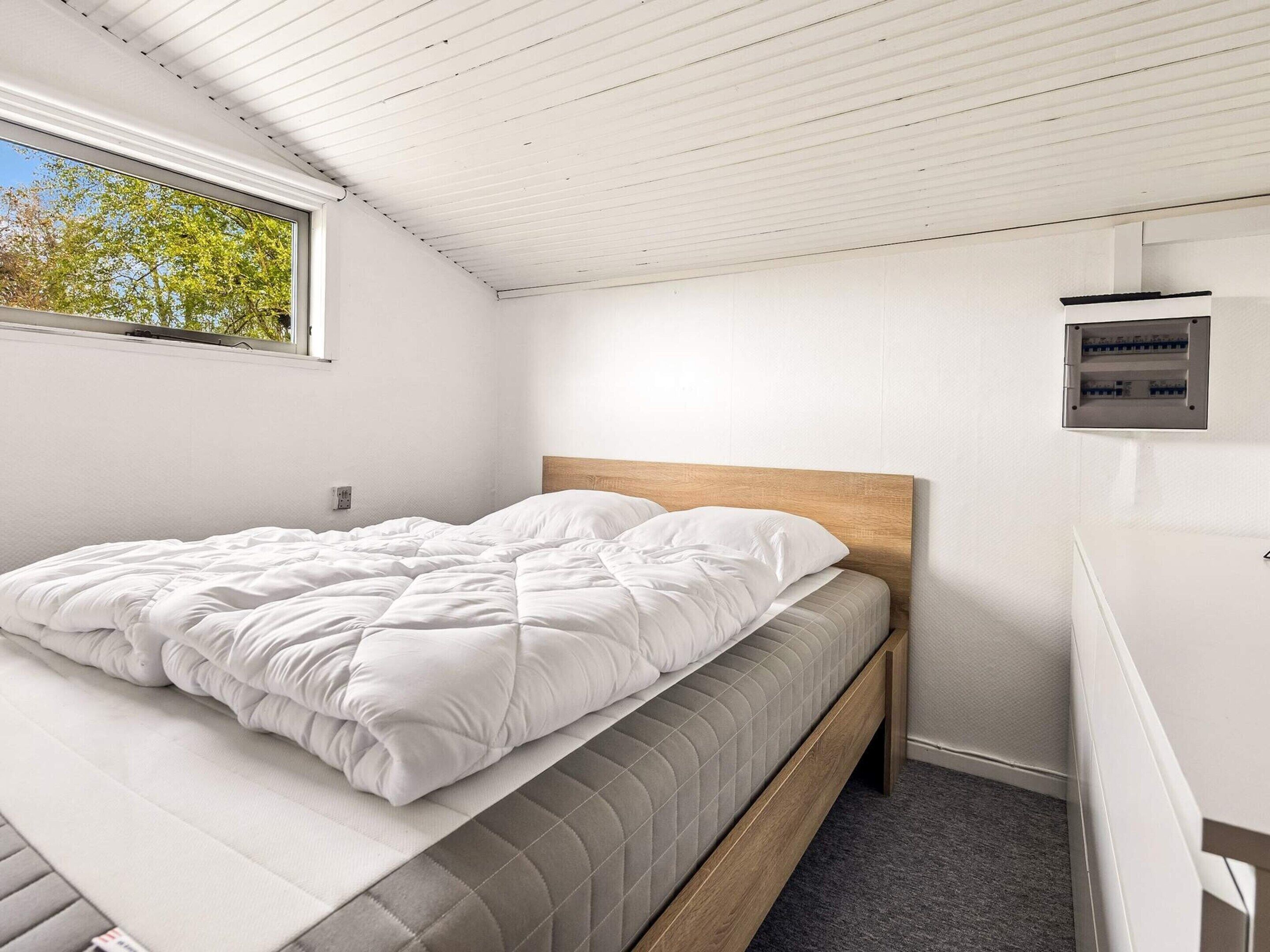 A bedroom with a bed, a wooden headboard, a window, and a wall-mounted electrical panel.