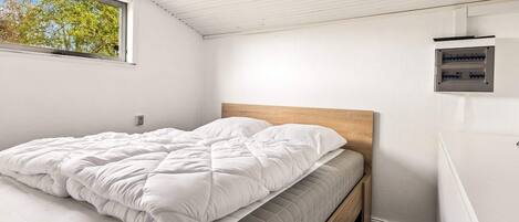 A bedroom with a bed, a wooden headboard, a window, and a wall-mounted electrical panel.