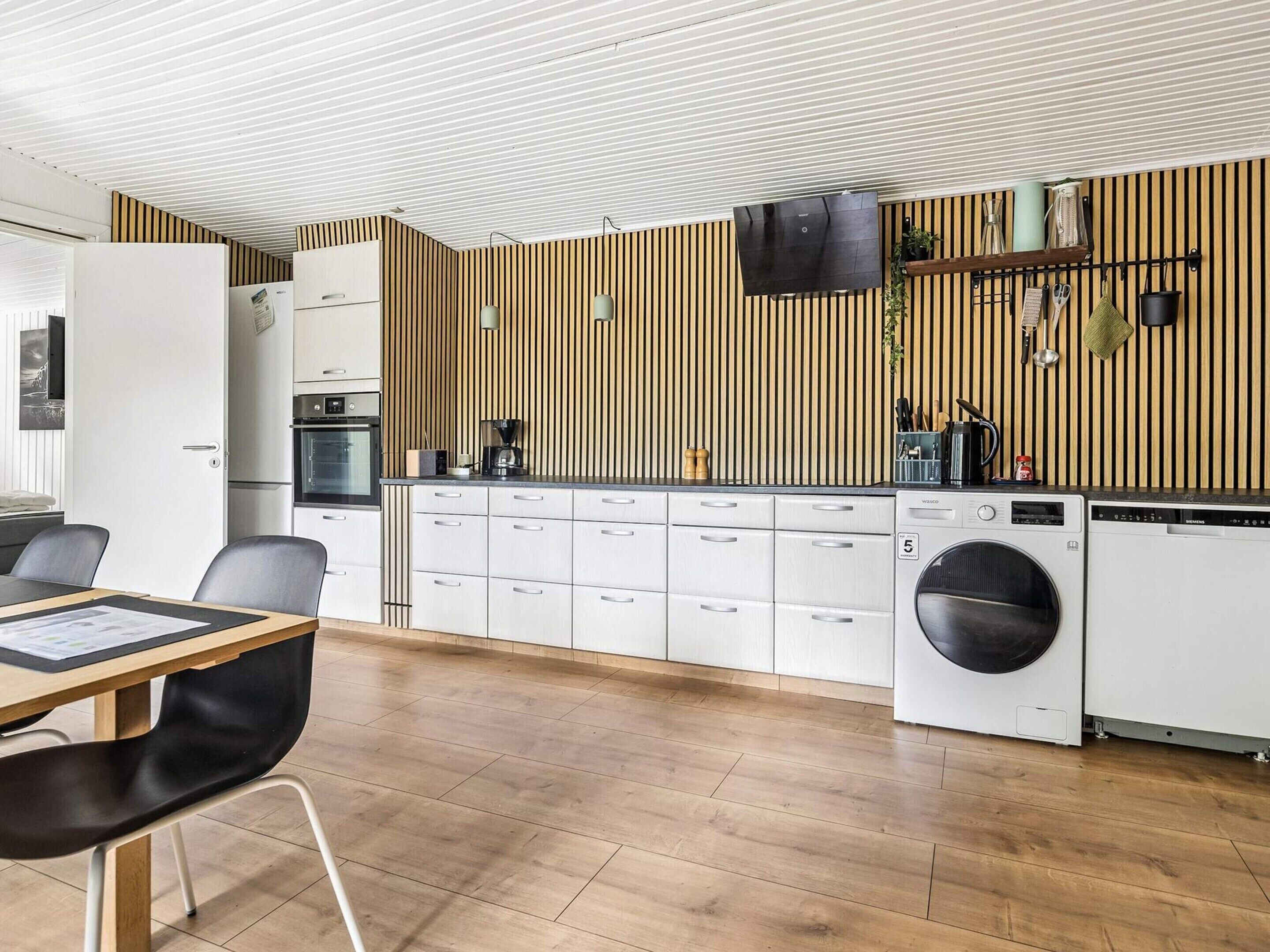A modern kitchen with a built-in washing machine, a dining area with a table and chairs, and a striped wall design.