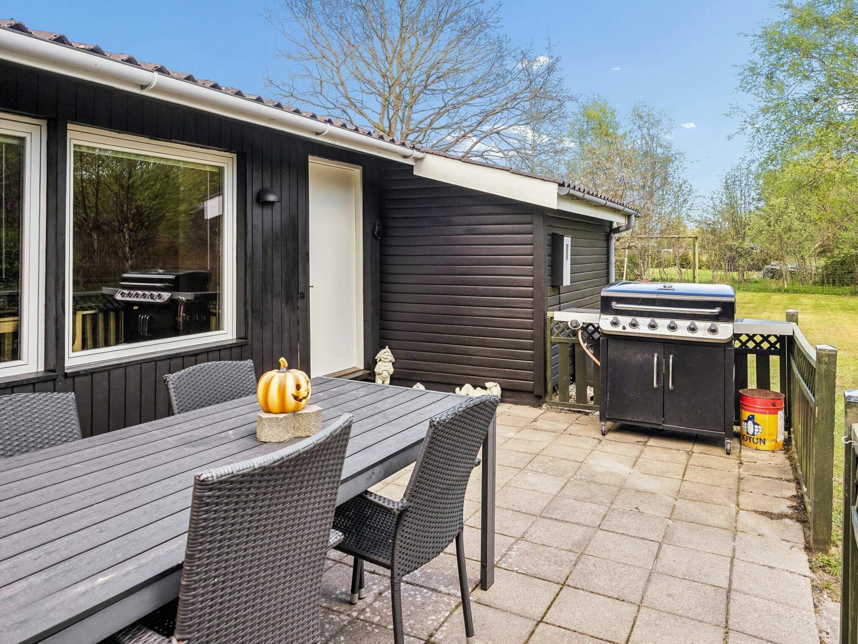 An outdoor patio with a table and chairs, a grill, and a decorative pumpkin.