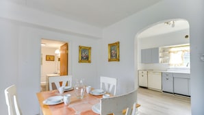 A dining area with a wooden table set for four, white chairs, and a kitchen in the background. - Main St Apt w/ Pool Table & Sauna in Westernport! (Westernport)