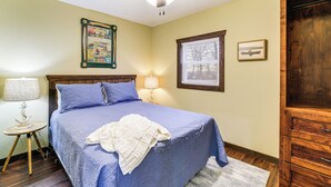 A bedroom with a bed, two bedside lamps, a ceiling fan, a framed picture on the wall, and a wooden cabinet. - Stunning Views! Table Rock Lake Cabin Near Marina (Shell Knob)