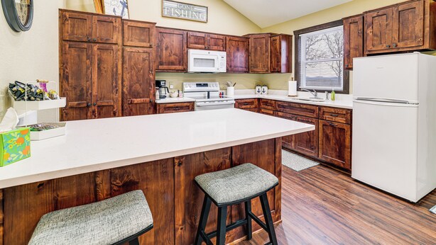 A kitchen with wooden cabinets, a white island with stools, a microwave, and a refrigerator. - Stunning Views! Table Rock Lake Cabin Near Marina (Shell Knob)