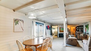 Een ruime kamer met een houten eettafel en stoelen, een comfortabele bank en een groot raam.