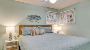 Une chambre dotée d’un grand lit, de deux tables de chevet avec des lampes, d’un ventilateur de plafond et d’œuvres d’art décoratives murales.