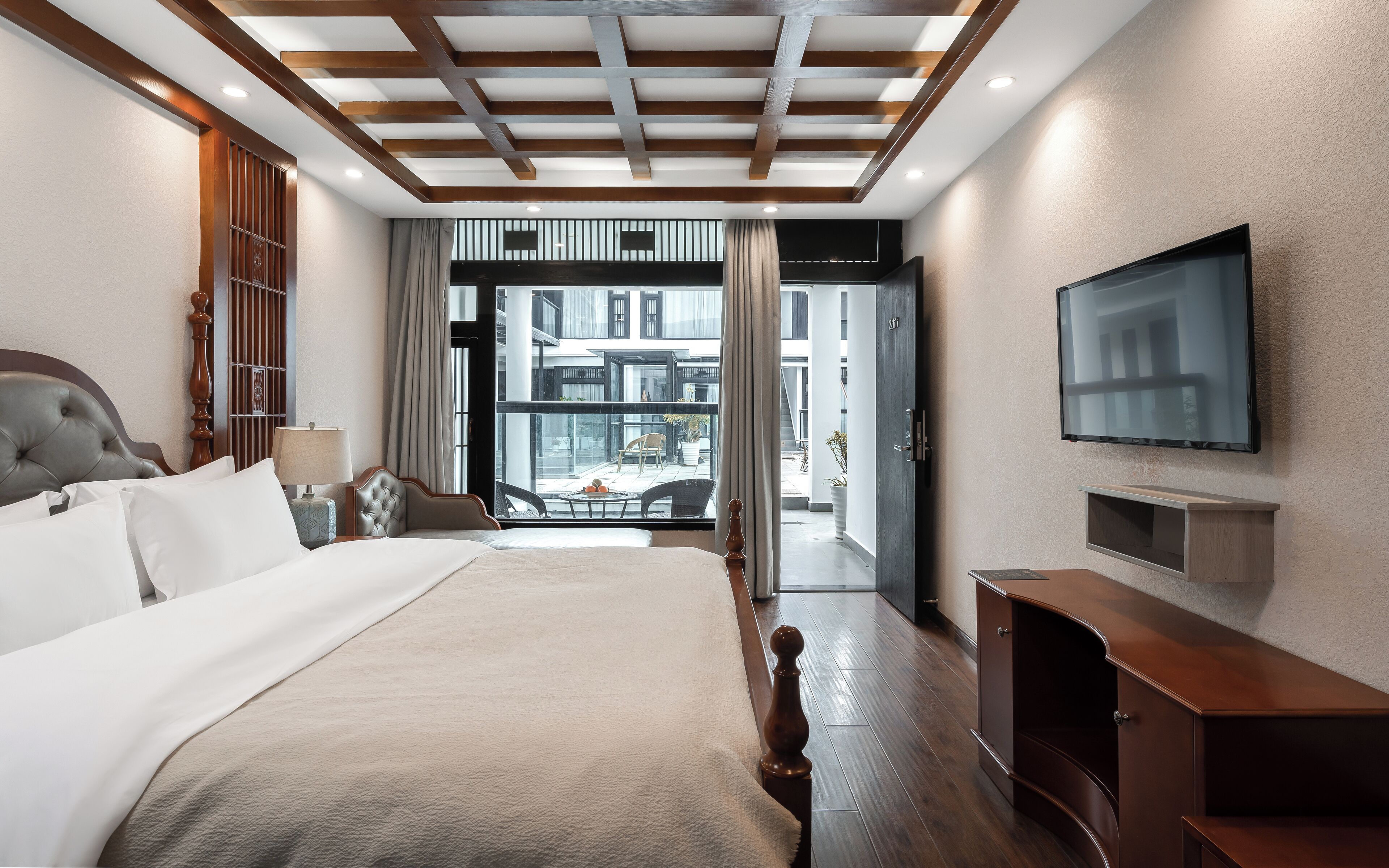 A hotel room with a large bed, a TV mounted on the wall, and a view of the outside balcony.