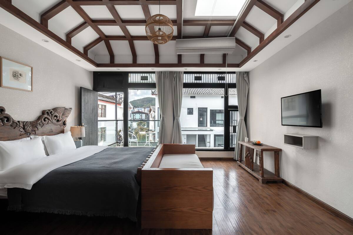 Un dormitorio moderno con una cama grande, televisión y balcón con vistas a edificios.