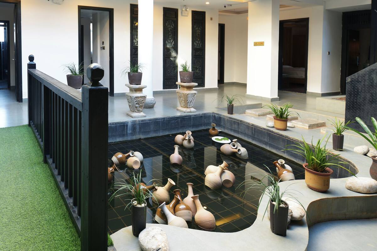 Un moderno vestíbulo de hotel con una fuente central rodeada de plantas en macetas y detalles de piedra.