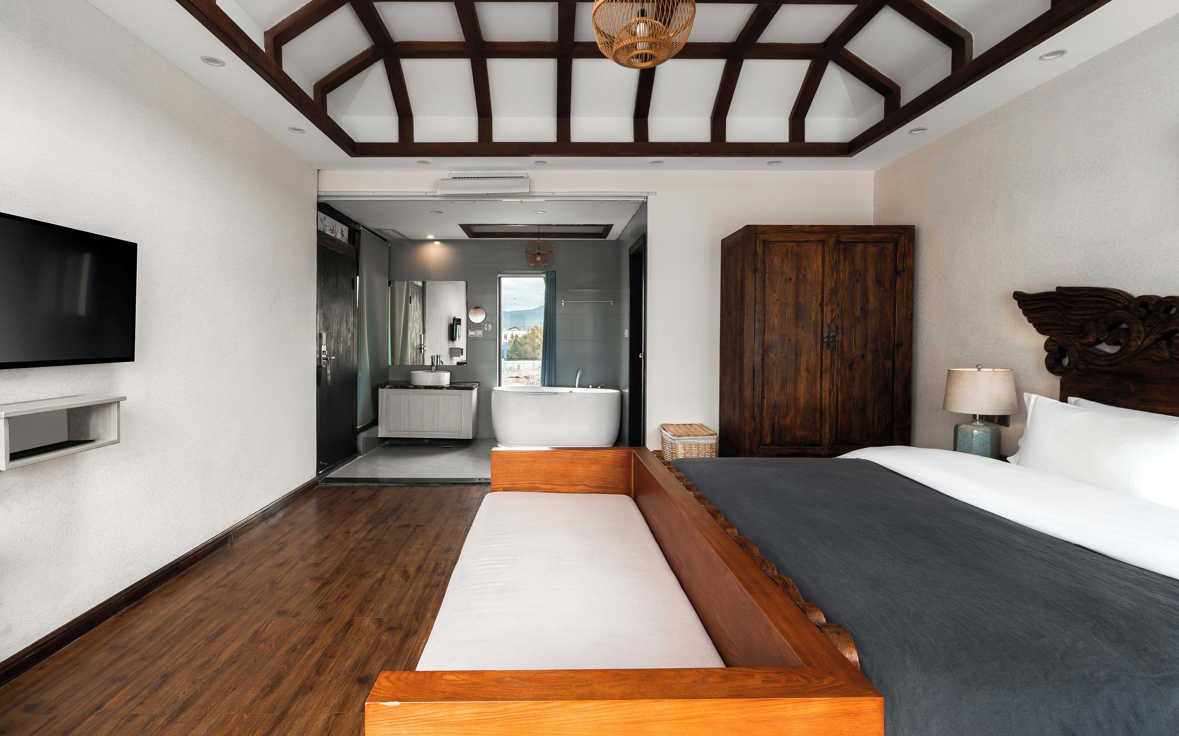 A modern hotel room with a large bed, a TV, a wooden headboard, and a view of the outdoors.