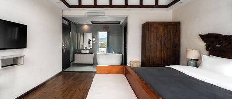 A modern hotel room with a large bed, a TV, a wooden headboard, and a view of the outdoors.