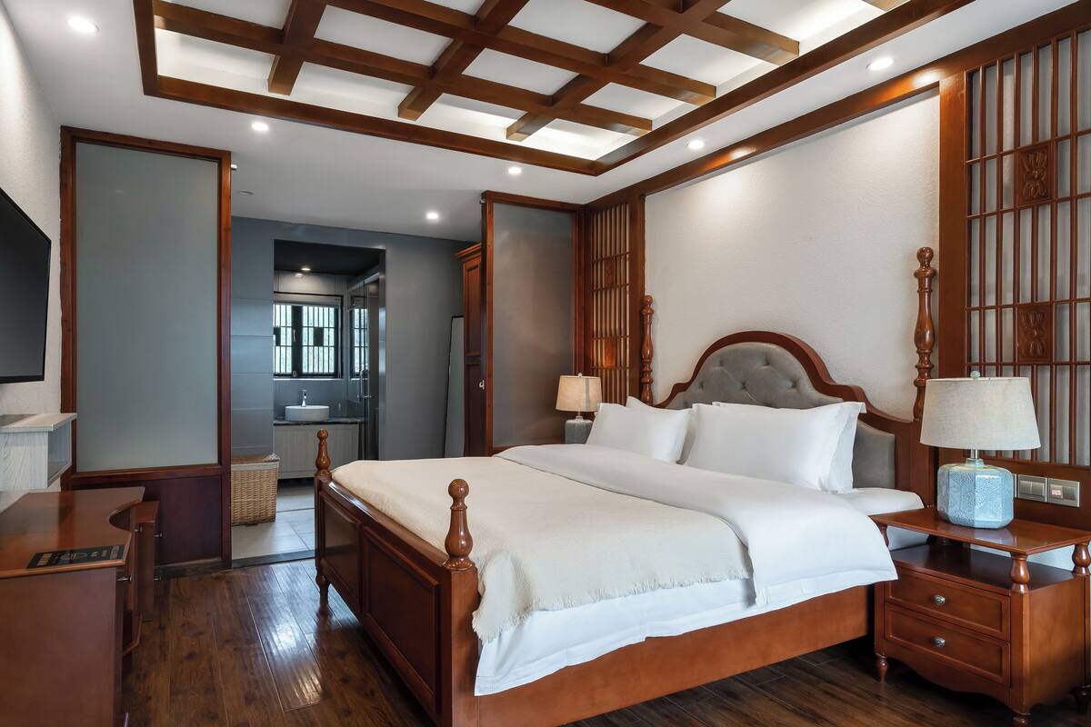 Un dormitorio con una cama grande, cabecera de madera, mesitas de noche, un escritorio y un televisor.