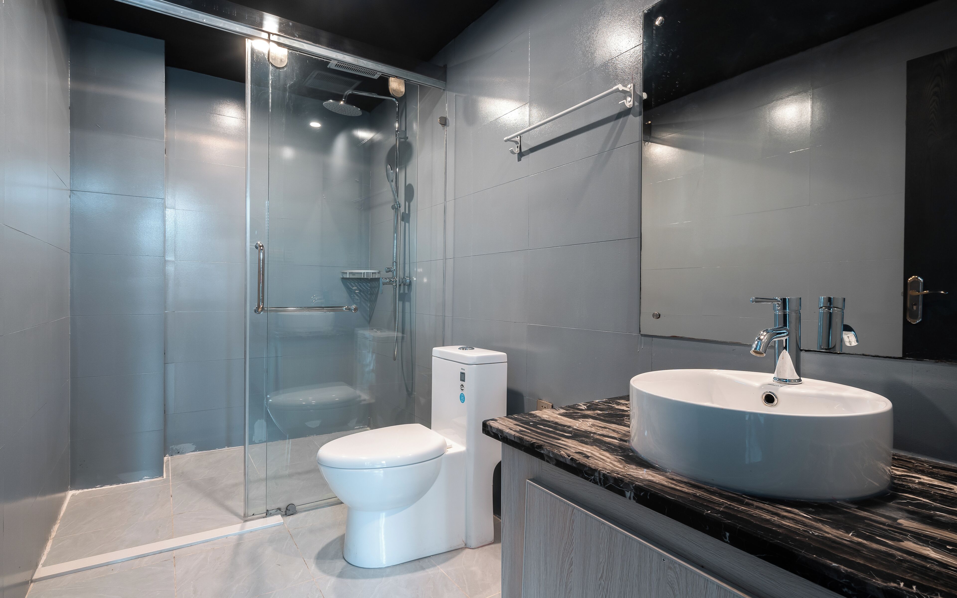 Une salle de bain moderne avec une douche à parois de verre, des toilettes blanches et un lavabo sur un plan de travail en marbre.