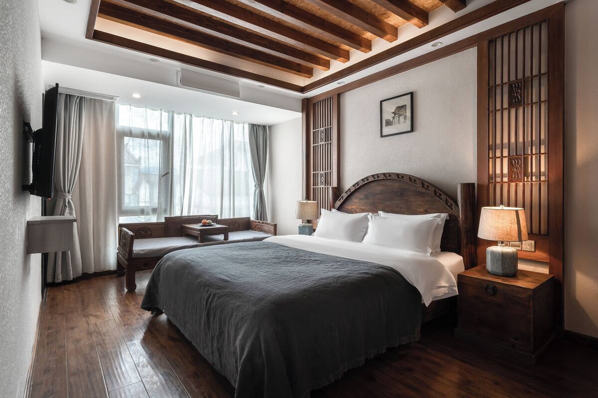 Habitación de hotel con una cama grande, mesitas de noche, un escritorio y una ventana con cortinas.