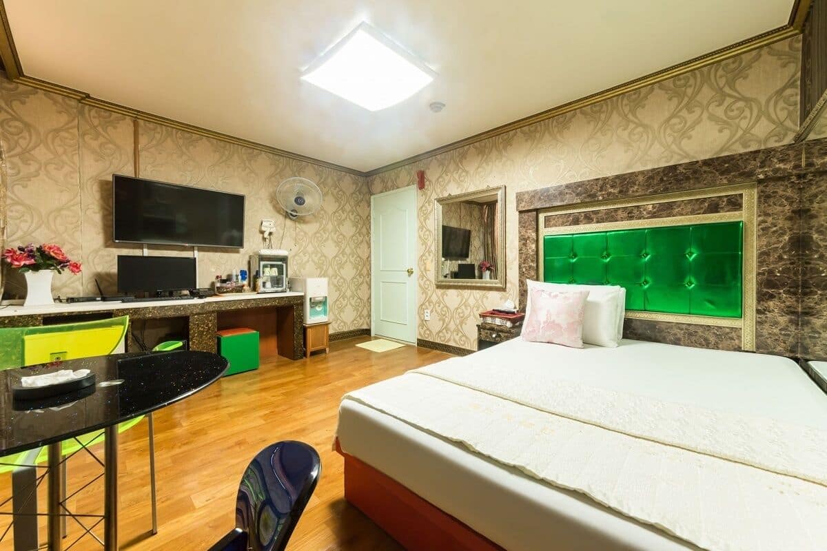A hotel room with a bed, a desk with a computer, a chair, and a TV.
